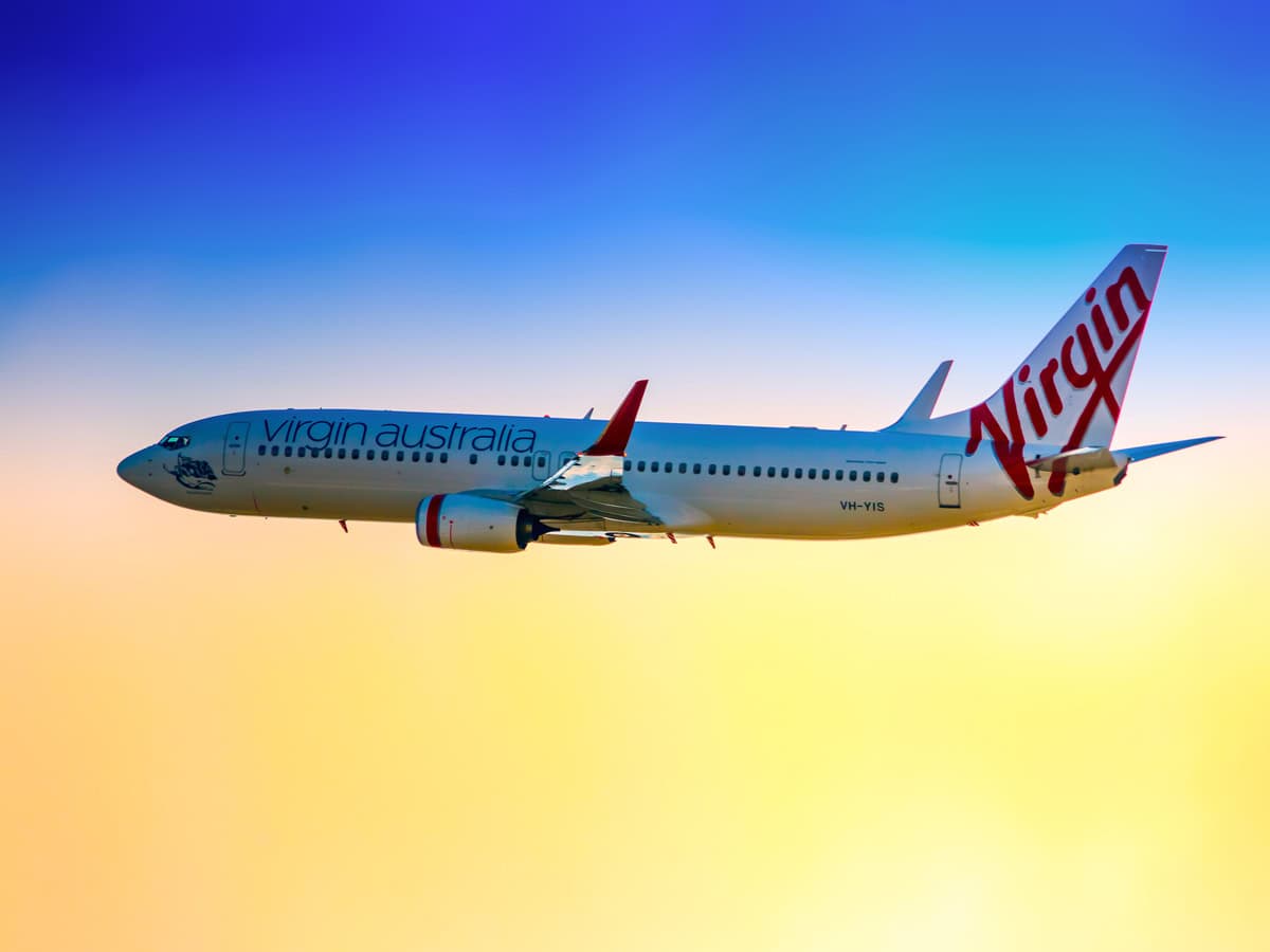 a Boeing 737-800 in Virgin Australia colour scheme taking off from Sydney (Kingsford Smith) Airport on a late afternoon. The plane is bound for Gold coast Queensland