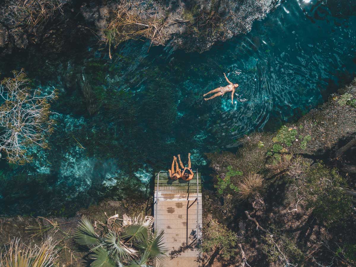 an aerial shot of a girl floating and two girls sitting on the edge of Mataranka Thermal Pool